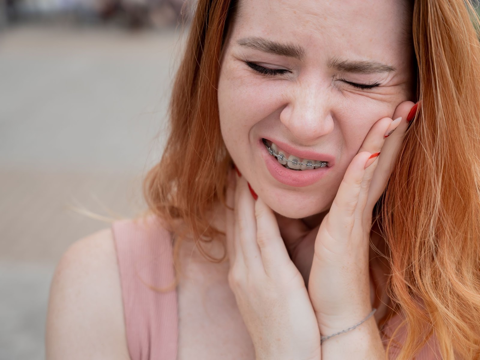 Young woman with braces holding her jaw in discomfort, illustrating the challenges of maintaining braces and potential issues like loose brackets or wires.