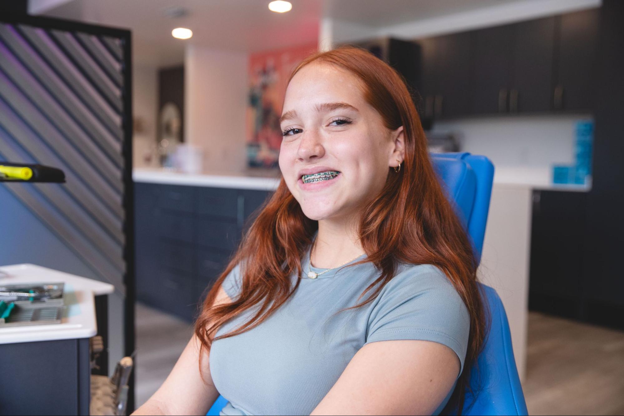 Smiling girl with braces sitting in an orthodontic chair at Orthodontics of South Miami, showcasing a welcoming dental office environment.