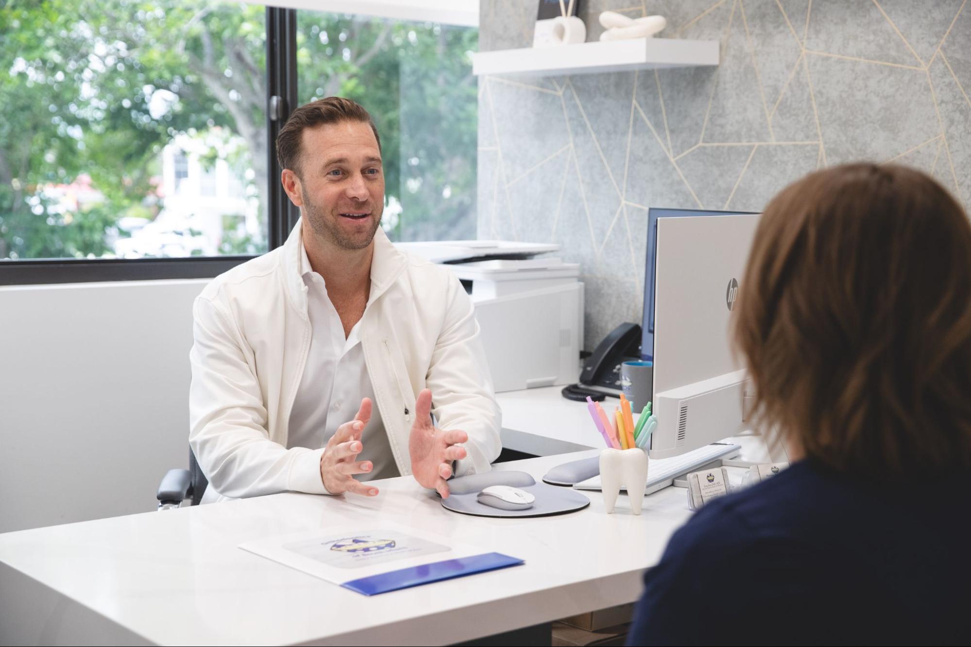 Orthodontist Dr. Ross consulting with a patient in a modern office setting, discussing treatment options like Invisalign and braces.